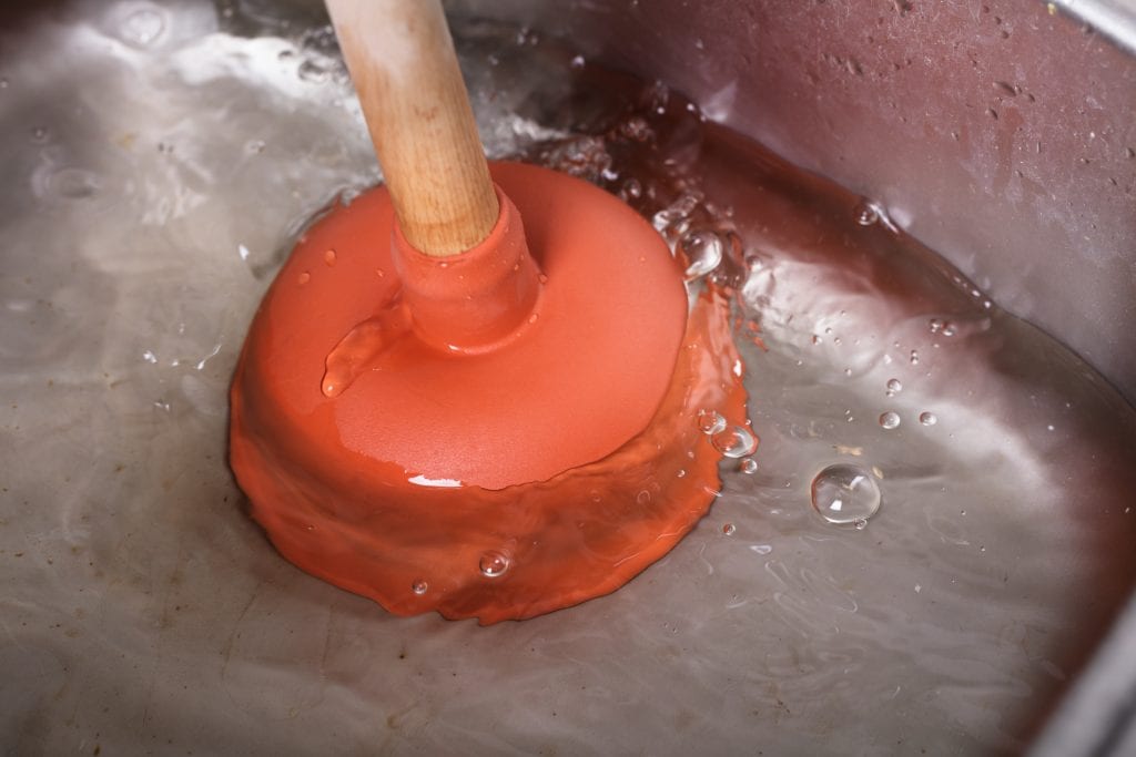 An Orange Plunger Being Used yo unblock a Sink In a Washbasin Filled With Water